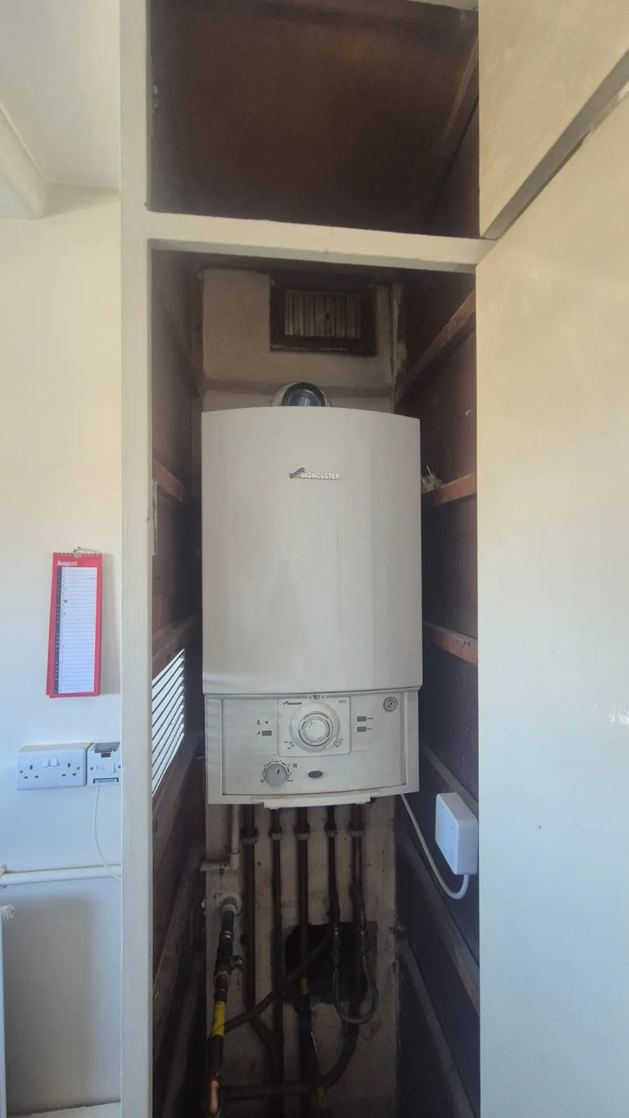 Cupboard doors off, showing the old unit in context and the pipework running below it.