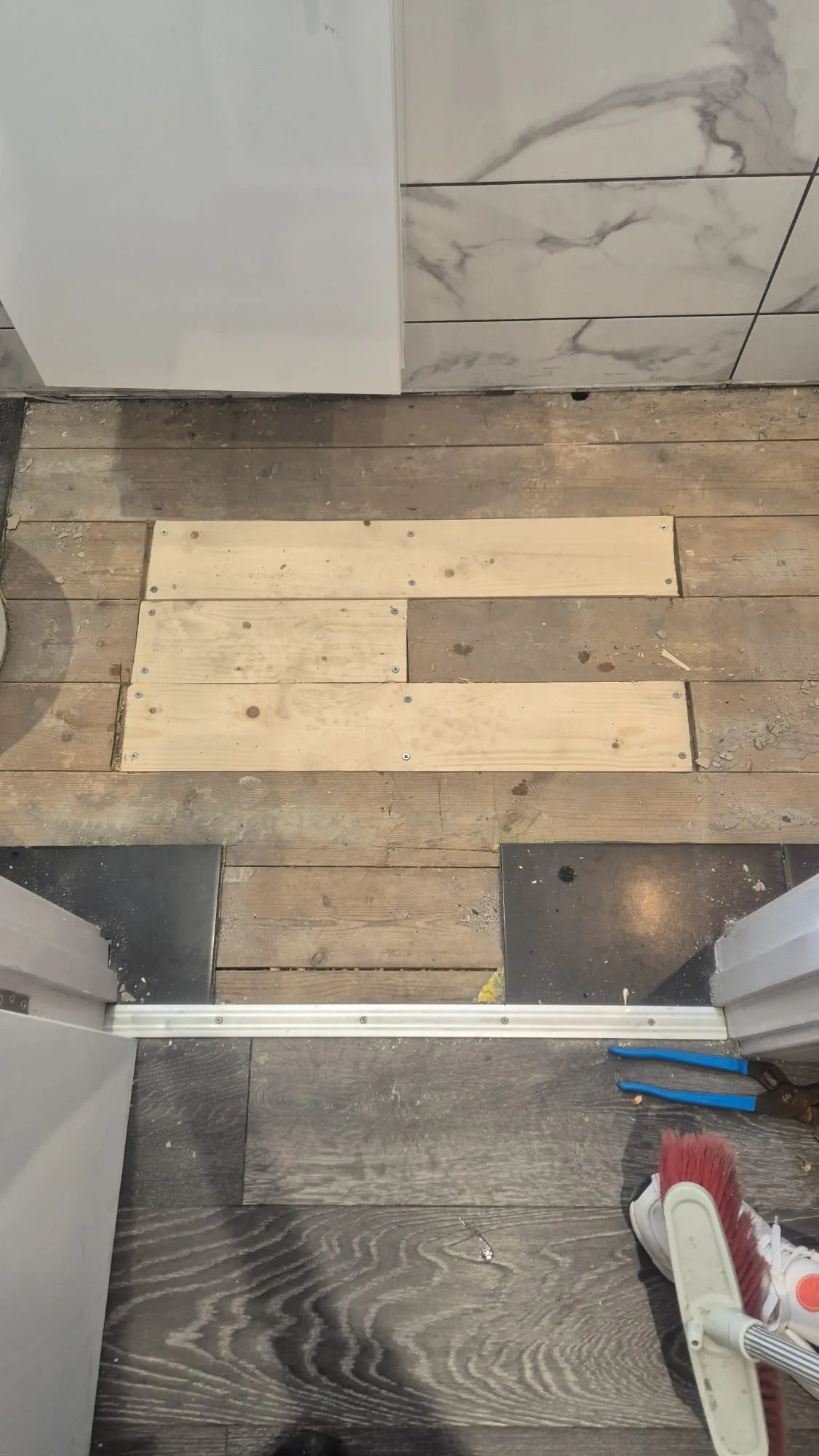 New boards cut and screwed down over the opening — square and flush, so the tiling has something sound to sit on.