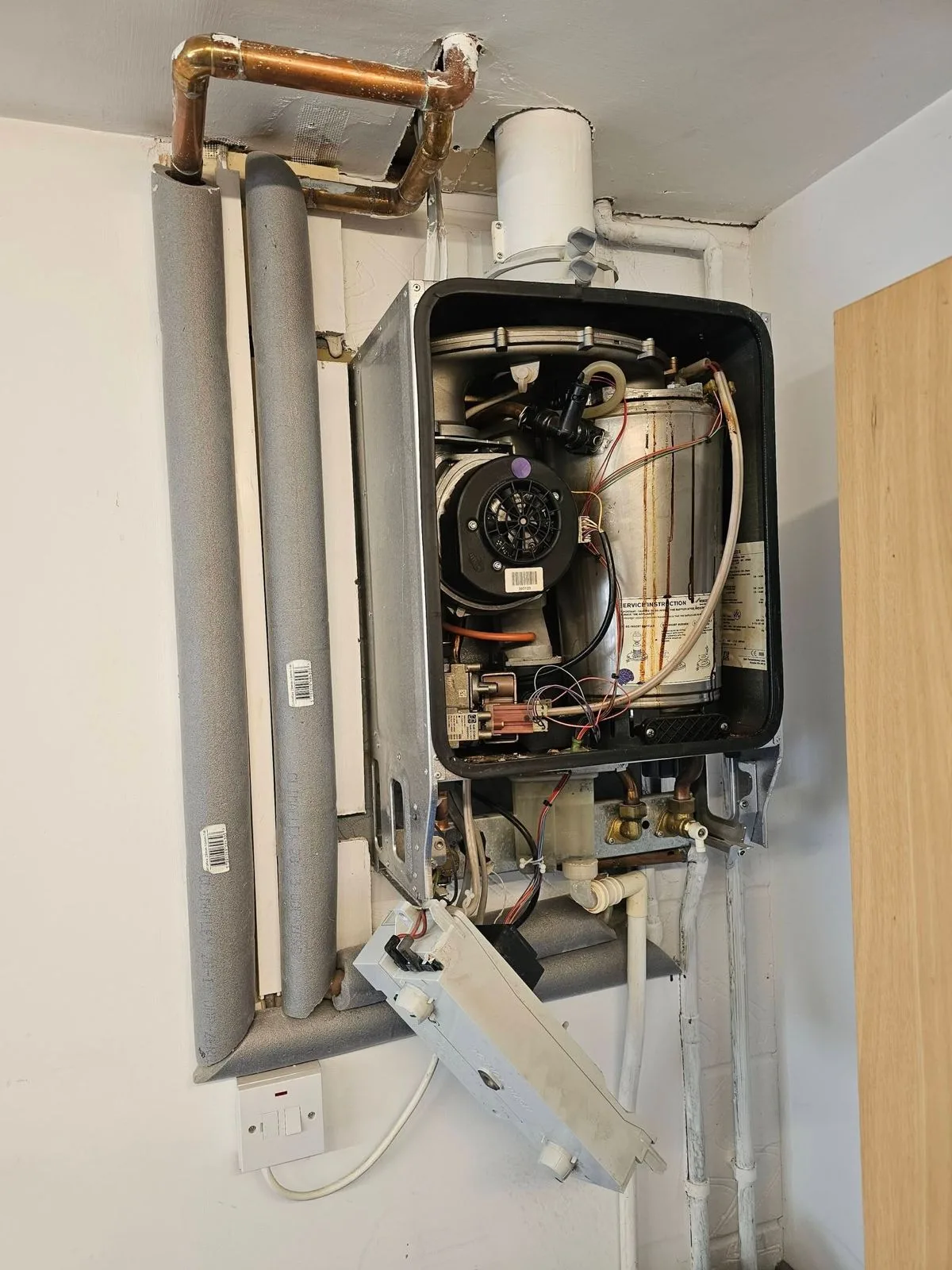 The old unit with its case off. The aluminium heat exchanger is heavily rust-stained down the face — this is the point where a repair stops making sense.