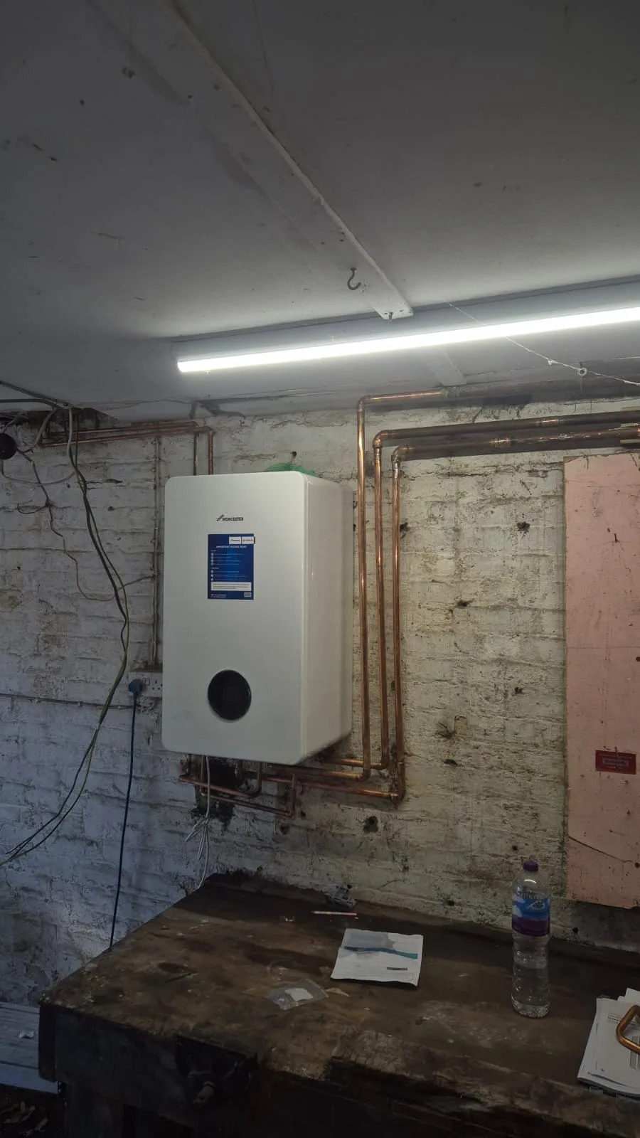Boiler mounted, protective film still on, with new copper runs up the wall and across at ceiling level.